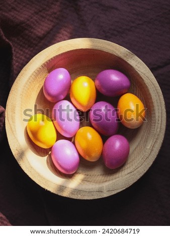 Colorful Easter eggs in a wooden plate on a dark burgundy kitchen towel.