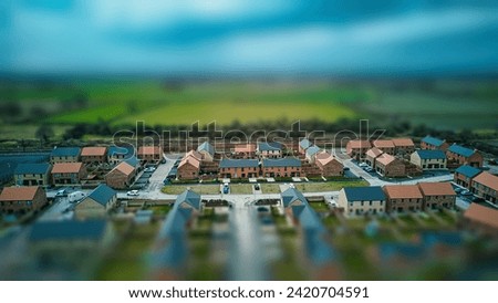 Tilt-shift aerial view of a suburban neighborhood with houses and roads, creating a miniature effect. Royalty-Free Stock Photo #2420704591