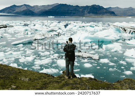 Man takes pictures of glacial lagoon and mountains on cell phone