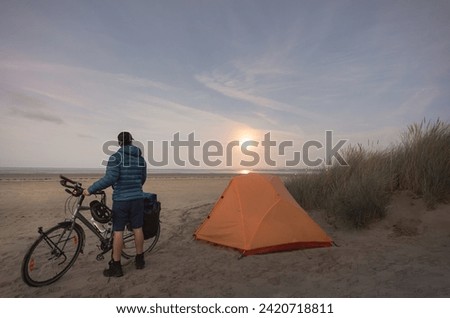 man with touring bike camping on beach under full moon
