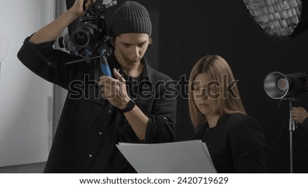 The director and cameraman review the script and discuss the upcoming shoot. A man with a professional video camera listens attentively to a woman who shows him the script and the layout of the shoot.