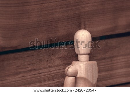 A wooden mvneken peeps into the sheel of a wooden fence, voyeurism. Royalty-Free Stock Photo #2420720547