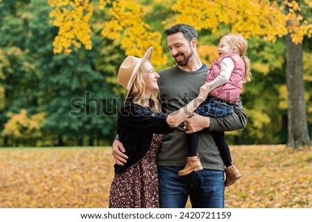Family of three laughing and embracing amid a fall backdrop