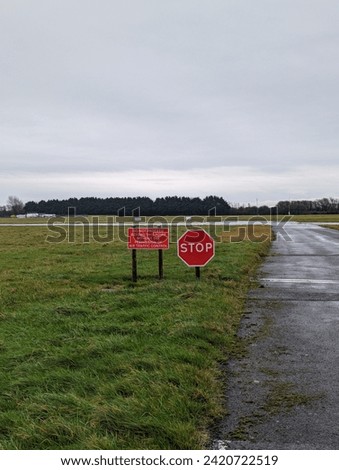 A solitary stop sign stands against the vast expanse of an open field, its bold red letters commanding the attention of passing cars on the quiet road