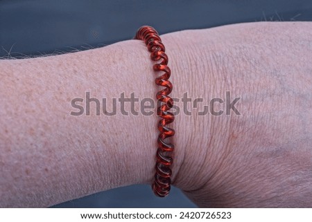 one red plastic bracelet made of wire on a white hand on a black background