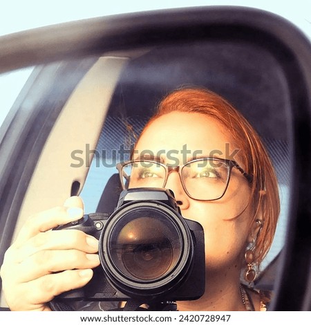 Photo of the sunset reflected in the lens of a camera and in the glasses of a woman with copper-colored hair.
