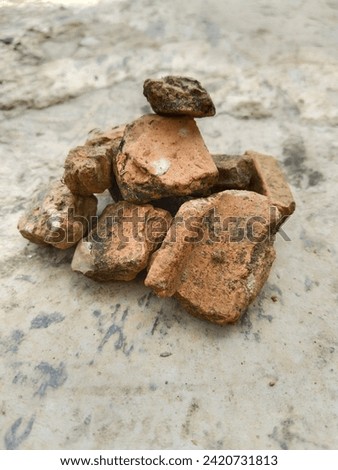 a picture of several stones and roof tile fragments arranged or stacked together to form a mountain or triangle on a gray cement floor.