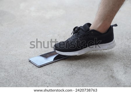 Closeup man wear black shoe, step on smartphone on ground, cause it crack. Concept, damage with things in daily life from accident or careless. Mobile phone warranty claim for broken                  