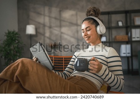 One young woman female sit at home use digital tablet and headphones to watch movie or series online stream or to have video call happy smile have a good time copy space