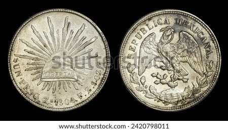 Large Mexican 1-peso coin with Phyrgian cap marked LIBERTAD on top of sunburst and 1904 on the front and coat of arms with cactus, eagle, and snake on back. Has more silver than U.S silver dollar. Royalty-Free Stock Photo #2420798011