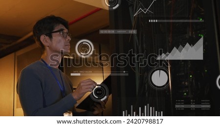 Image of processing circles and graphs over asian man working in server room. network, programming, computers and technology concept digitally generated image.