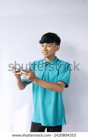 Portrait of attractive Asian man in blue t-shirt playing games on his mobile phone by tilting the screen. Wow face expression. Isolated image on white background