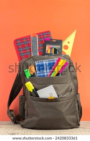 Backpack with different colorful stationery on table. Orange background. Back to school