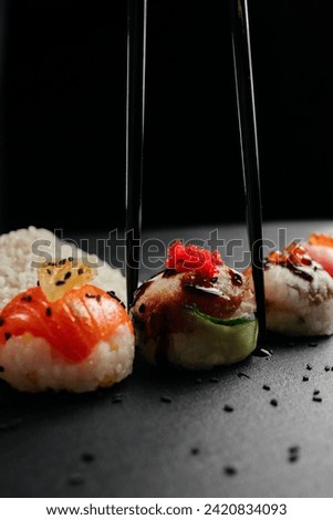 Variety of bright sushi rolls with greens on a black background. Incredible fresh sushi rolls on a dark background. Cooking traditional Japanese seafood and fish dishes.