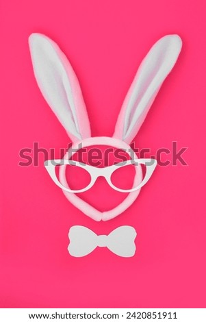 Easter bunny ears headband with glasses and bow tie on vivid pink background. Abstract surreal crazy minimal fun design for the holiday season.