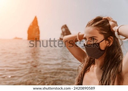 Woman summer travel sea. Happy tourist in black mask enjoy taking picture outdoors for memories. Woman traveler posing on the beach at sea surrounded by volcanic mountains, sharing travel adventure