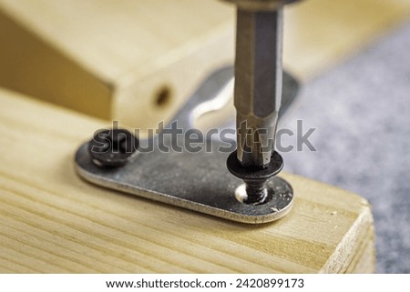Screwing a furniture hanger to a board with a self-tapping screw, close-up. Selective focus Royalty-Free Stock Photo #2420899173