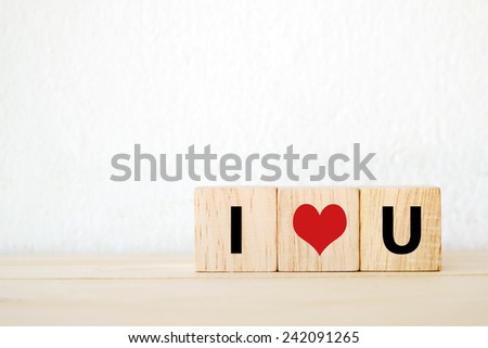 Three wood cubes with " I love you " words on wooden table over white cement wall, valentine background template