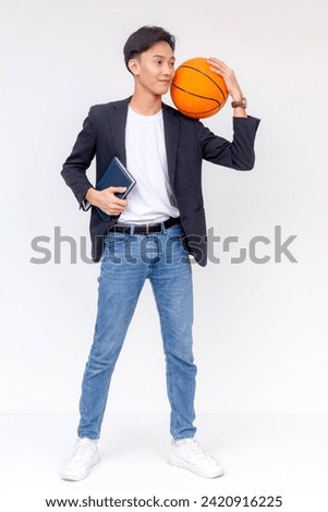 A stylish young man in business attire holds a basketball while gripping a planner, portraying a blend of professional and athletic life.