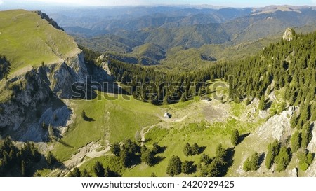 Aerial drone panorama above a steep valley and a rocky mountain crest on which a wooden sheepfold was built. Autumn season, the woodlands are colored in yellow. Carpathia, Romania. Royalty-Free Stock Photo #2420929425