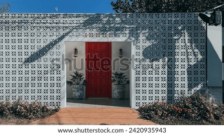 The white brick design  symmetry red door between classic lamp  chinese pot with plant  shadow on the wall in front the building  cute flower like a little garden all is nice object