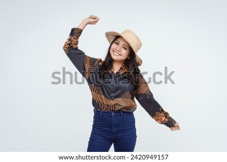 Cheerful female with a radiant smile wearing a straw hat and patterned shirt against a light background.