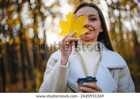 Beautiful young woman walks in the autumn park and drinks coffee from paper cup