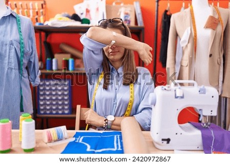 Hispanic young woman dressmaker designer at atelier room covering eyes with arm, looking serious and sad. sightless, hiding and rejection concept  Royalty-Free Stock Photo #2420972867