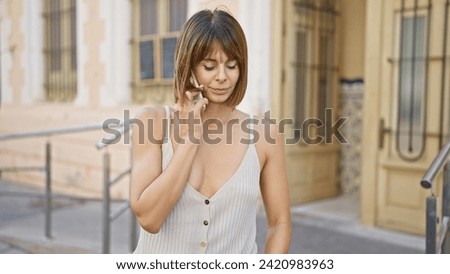 Stunning young hispanic woman holding a serious, focused, conversation on her smartphone while standing coolly on a sun-soaked city street. Royalty-Free Stock Photo #2420983963