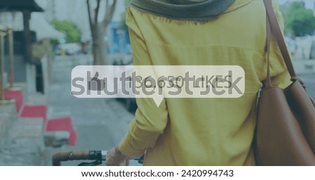 Image of like symbol with rising number and woman in hijab wheeling bike in city street. communication technology digital interface concept, digitally generated image.