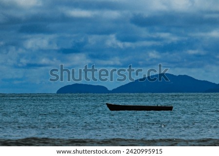 rowing boat anchored off the beach, in a sea of ​​green waters, in the background of the Serra do Mar mountains.