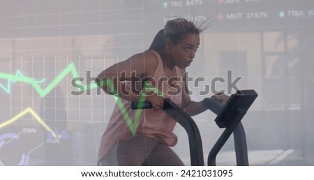 Image of data processing on graph over biracial woman cross training on elliptical at gym. Fitness, exercise, strength, data, digital interface and technology digitally generated image.