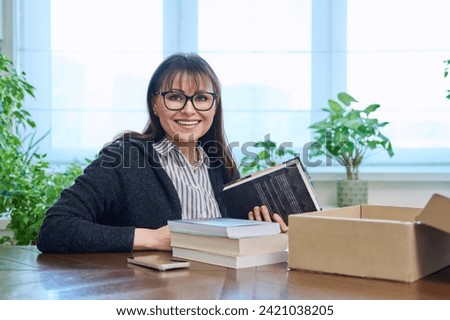 Middle-aged joyful woman with new books unpacked from cardboard box Royalty-Free Stock Photo #2421038205