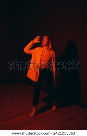 A model makes a bold statement, her hand raised against a deep red backdrop, casting an shadow