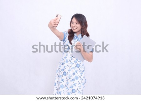 beautiful asian woman wearing modern chinese blue dress obliquely cheerful holding tablet and photo looking at cellphone isolated white background