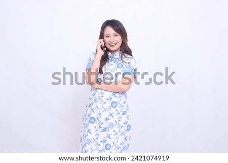 Young Asian Javanese Chinese woman laughing wearing blue Chinese dress while on the phone looking at camera isolated white background