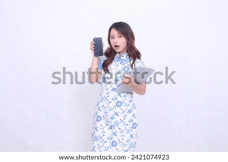 Beautiful Asian woman wearing blue Chinese dress holding tablet and looking at cellphone screen isolated on white background