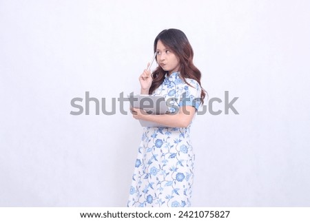 beautiful Indonesian Chinese woman thinking wearing modern Chinese blue dress carrying tablet view top right isolated white background
