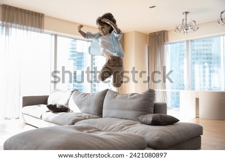 Happy vivacious adorable little boy jumping on soft couch play alone at home, having fun, fooling, spend carefree leisure in up-to-date living room studio apartments. Hyperactivity, games, childhood Royalty-Free Stock Photo #2421080897