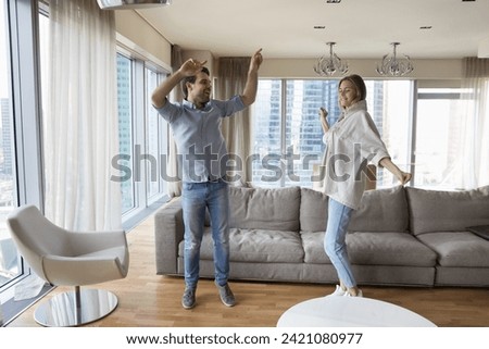 Happy couple dancing in modern living room, spend carefree leisure in skyscraper apartment, celebrate relocation day, enjoy dating, listen music, lively moving. Tenancy, hobby, bank mortgage, new flat Royalty-Free Stock Photo #2421080977