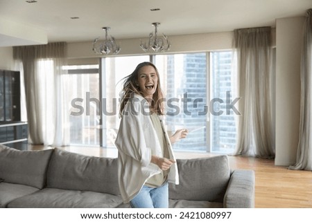 Lively young beautiful woman having fun, dancing alone in living room, sing favourite song, enjoy carefree pastime, day off or holidays in modern own or rented apartment. Bank loan, tenancy, leisure Royalty-Free Stock Photo #2421080997