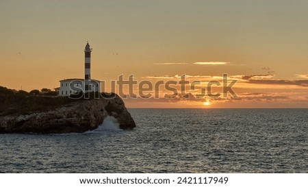 Seagulls fly by the Porto Colom lighthouse on the island of Mallorca at dawn