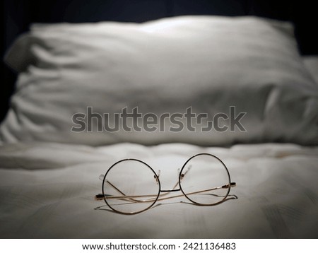 An eyeglasses optics on white linen bed, low light night time, shortsighted, nearsighted, farsighted, eyewear business products, relax or rest or sleeping time concept, focus on foreground Royalty-Free Stock Photo #2421136483