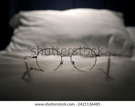 An eyeglasses optics on white linen bed, low light night time, shortsighted, nearsighted, farsighted, eyewear business products, relax or rest or sleeping time concept, focus on foreground Royalty-Free Stock Photo #2421136485