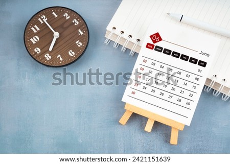 2024 June calendar page and wooden clock on blue wooden background.