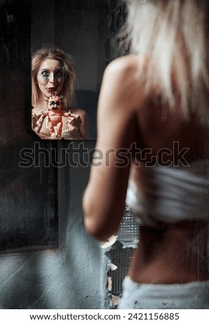 Strange mad girl with scary ugly doll in forsaken place (madhouse). Insane smiling young woman (freak) looking into mirror. Portrait of the mental sick (schizophrenic). Grunge texture added Royalty-Free Stock Photo #2421156885