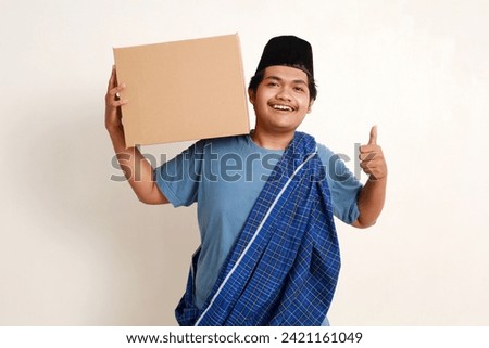 Happy asian muslim boy standing showing thumbs up while carrying a package