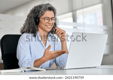 Happy mature business woman call centre representative customer support agent talking to client, smiling middle aged senior female operator wearing headset working using laptop computer in office. Royalty-Free Stock Photo #2421190759