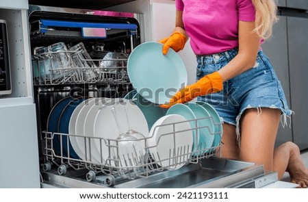 Young woman takes dishes out of the dishwasher machine