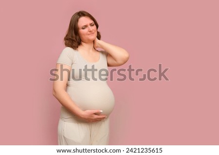 A pregnant woman holds onto a aching neck on a studio pink background. Pregnancy in a woman with a belly, copy space